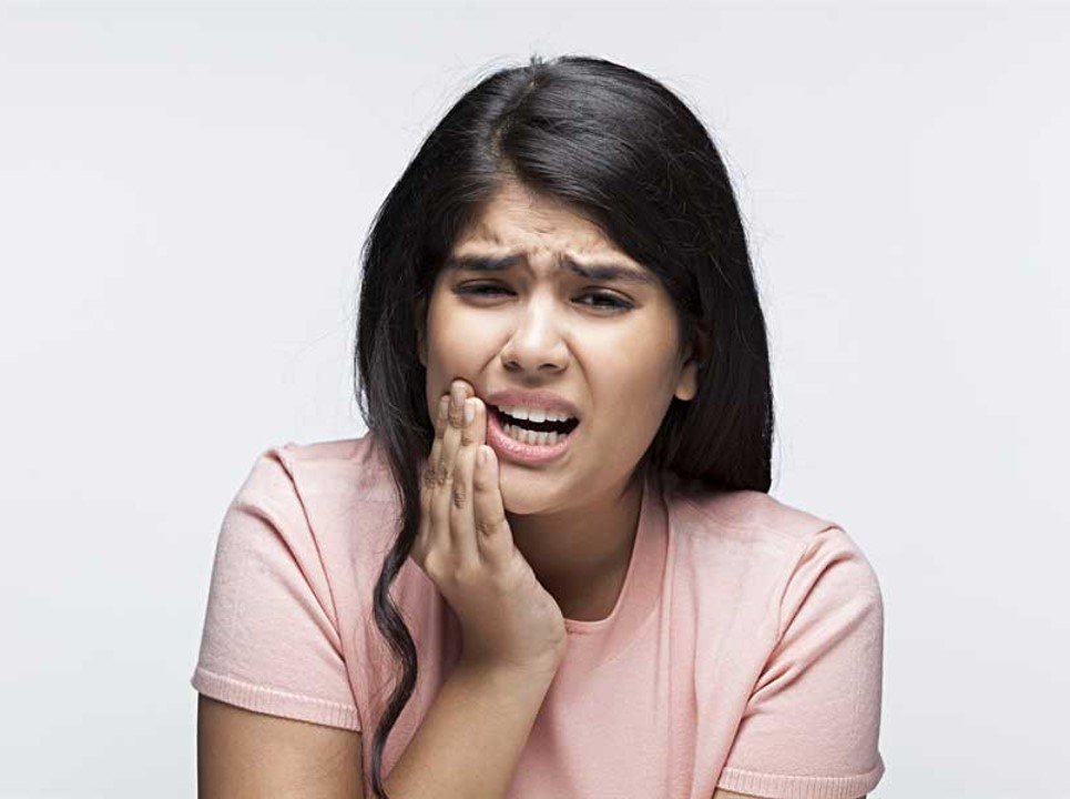 Woman holding her cheek while experiencing tooth pain.